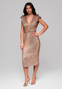 Abito in paillettes rosa oro con scollatura a V profonda, maniche a cappuccio e una silhouette aderente, abbinato a sandali open-toe con cinturino alla caviglia.