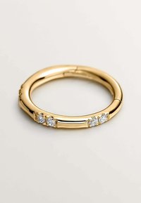 Anillo de oro con un diseño liso y redondeado, que presenta tres pequeñas piedras preciosas transparentes engastadas a lo largo de un lado, mostrando un acabado pulido.