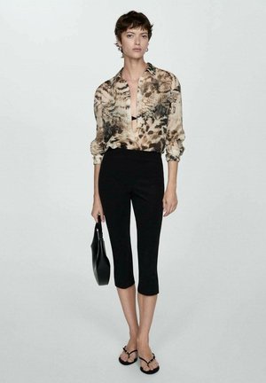 Ohut, kuviollinen toppi, jossa on eläinkuoset beige ja ruskea, yhdistettynä tiukkoihin mustiin capri-housuihin. Malli pitää mustaa laukkua.