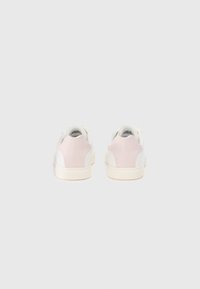Fehér sneakers, puha rózsaszín kiegészítőkkel, sima bőr felsőrésszel és texturált gumi talppal. Minimalista dizájn, logó a sarkán.