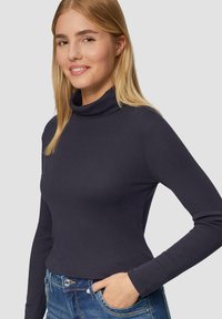 Dunkelblauer Rollkragenpullover aus weichem Material, mit langen Ärmeln und figurbetontem Schnitt, kombiniert mit blauen Denim-Jeans.