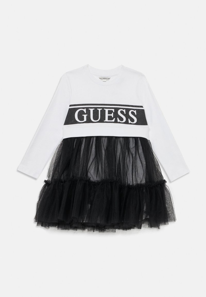 Vestido branco de manga longa com saia de tule preta, apresentando uma faixa com o logótipo "GUESS" preta no peito. O tule adiciona textura e volume.