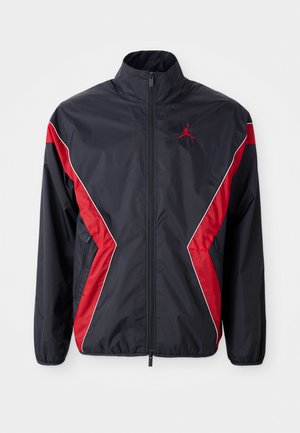 Giacca a vento in nylon nera e rossa con colletto alto, zip frontale e tasche laterali; presenta un design a blocchi di colore angolari e un dettaglio del logo.