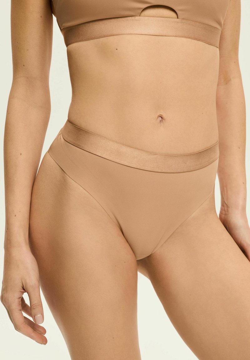 Beżowe, prążkowane bikini dolne z szerokim, gładkim pasem w talii. Materiał ma miękką teksturę, zaprojektowany dla wygody i dopasowania. Brak widocznych wzorów.