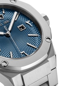 Reloj de acero inoxidable con un dial azul texturizado que presenta patrones de diamantes, marcadores de hora en plata y una ventana de fecha a las 3 en punto.