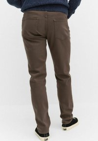 Bruna denimbyxor med rak skärning, bakfickor och en mjuk textur, i kombination med svarta skor med en krämfärgad sula.