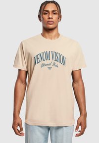 Bežs kokvilnas T-krekls ar zilu grafiku tekstu "VENOM VISION" un "Eternal Fate" stilizētā fontā. Īsas piedurknes, brīvs piegriezums.