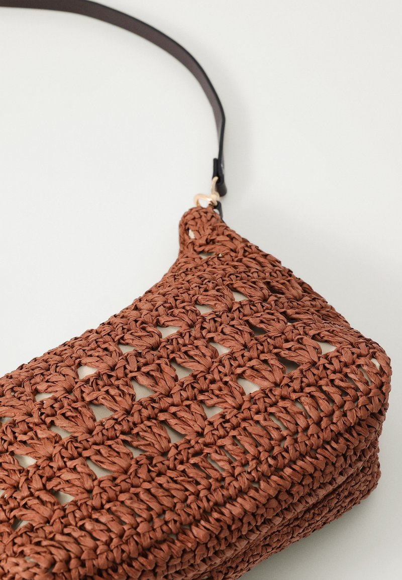 Bolso de mano tejido en marrón con un diseño de crochet texturizado y una correa negra elegante, que presenta secciones de malla abierta y una forma rectangular.