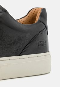 Czarne skórzane sneakersy o teksturowanej powierzchni, z beżowym perforowanym wykończeniem i białą gumową podeszwą. Posiadają wytłoczone logo z boku.