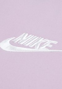 Vijoličasta tkanina z vezenim belim napisom "NIKE". Enostavna zasnova, gladka tekstura, brez dodatnih vzorcev ali poudarkov.