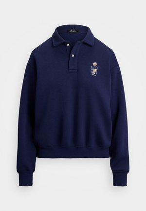 Paita sweatshirt tummansinisestä puuvillasta. Siinä on kauluspanta, kaksi nappia ja brodeerattu kuvio vasemmalla rinnalla.
