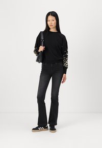 Svart hettegenser med blomsterbroderi på ermene, kombinert med vide svarte jeans og svarte sneakers med hvite striper. Inkluderer en svart veske.