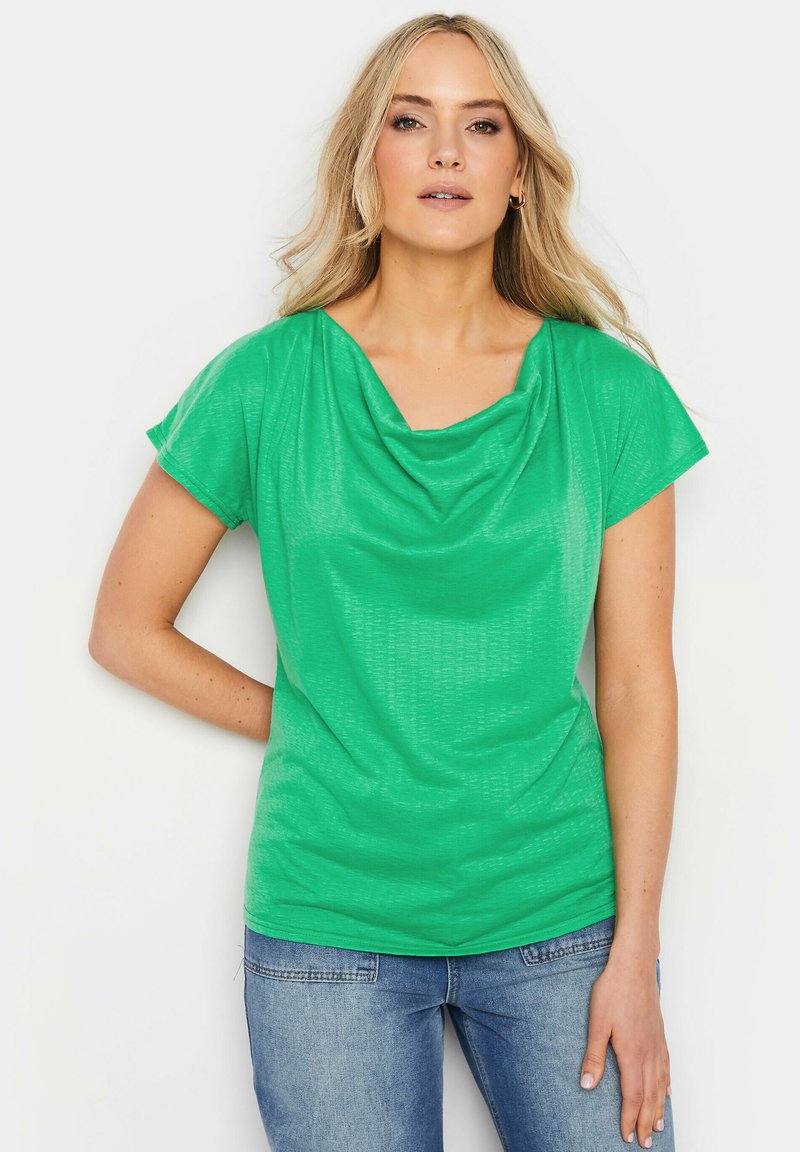 Top verde a maniche corte con scollatura a drappeggio e tessuto testurizzato. Abbinato a jeans azzurri chiari, presenta una vestibilità rilassata e una texture liscia.