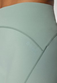 Leggings sportivi a vita alta in verde menta chiaro, realizzati in materiale liscio con cuciture piatte e logo "BORG" in rilievo.
