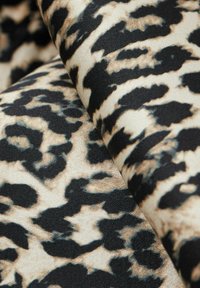 Pletteret stof med leopardmønster, der har en beige baggrund med mørkebrune og sorte pletter, og som viser en glat tekstur og blød fald.