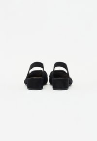 Sandales en suede noir avec un petit talon carré et une sangle arrière réglable, présentant un design ouvert à l'avant et une texture de surface lisse.