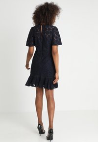 Navy lace dress with short sleeves, a flared hem, and a keyhole back detail. Finished with a textured lace pattern and fitted waist.