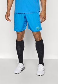 Blå sportshorts lavet af letvægtsstof, parret med sorte knælange sokker og hvide fodboldstøvler med sorte accenter.
