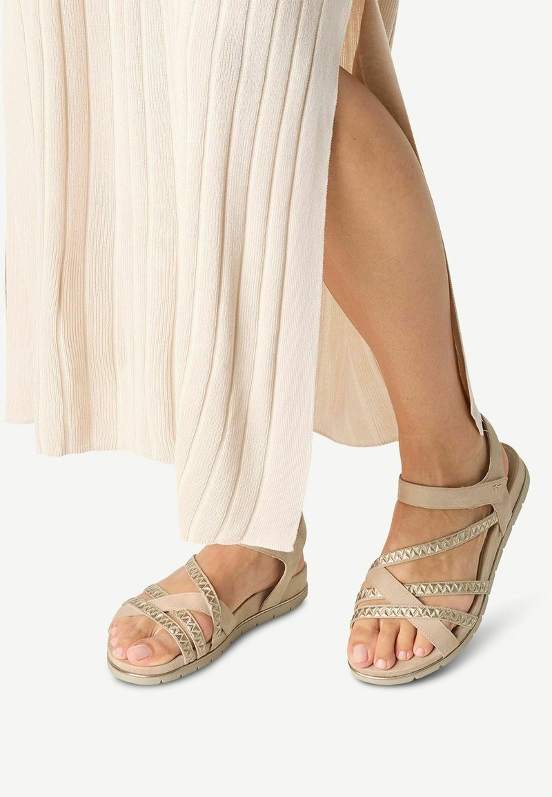 I sandali beige presentano cinghie morbide con un design incrociato e dettagli testurizzati, abbinati a una leggera gonna a pieghe.