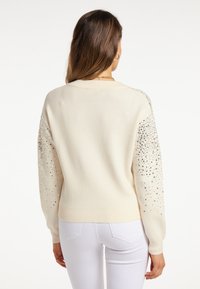 Maglione crema con scollatura arrotondata e tessuto strutturato. Maniche decorate con paillettes argento sparse, orlo e polsini a costine.