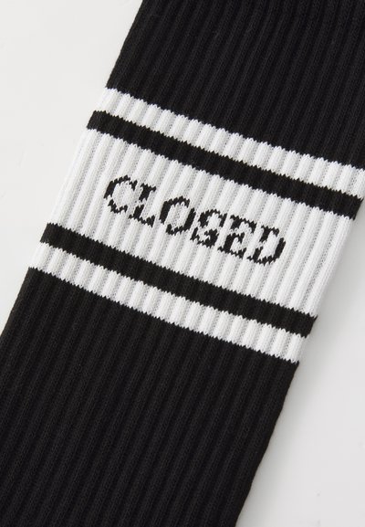 Black ribbed socks featuring two white horizontal stripes and the word "CLOSED" in black text across the upper section.