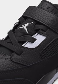 Κοντινό πλάνο μαύρου αθλητικού παπουτσιού Air Jordan με υφή δέρματος, κορδόνια, λευκό λογότυπο Jumpman και «JORDAN» χαραγμένο στο λουράκι.