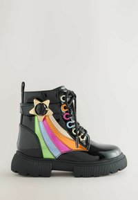 Botín negro de charol con rayas coloridas (rosa, naranja, azul, verde) y herrajes en forma de estrella. Presenta cordones negros y una suela texturizada.