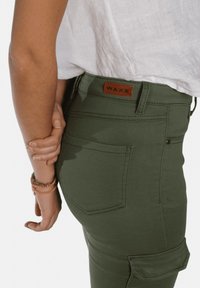 Pantalons cargo verts en mélange de coton, avec une poche appliquée, des poches arrière et une étiquette de marque en cuir. Texture lisse avec une coupe ajustée.