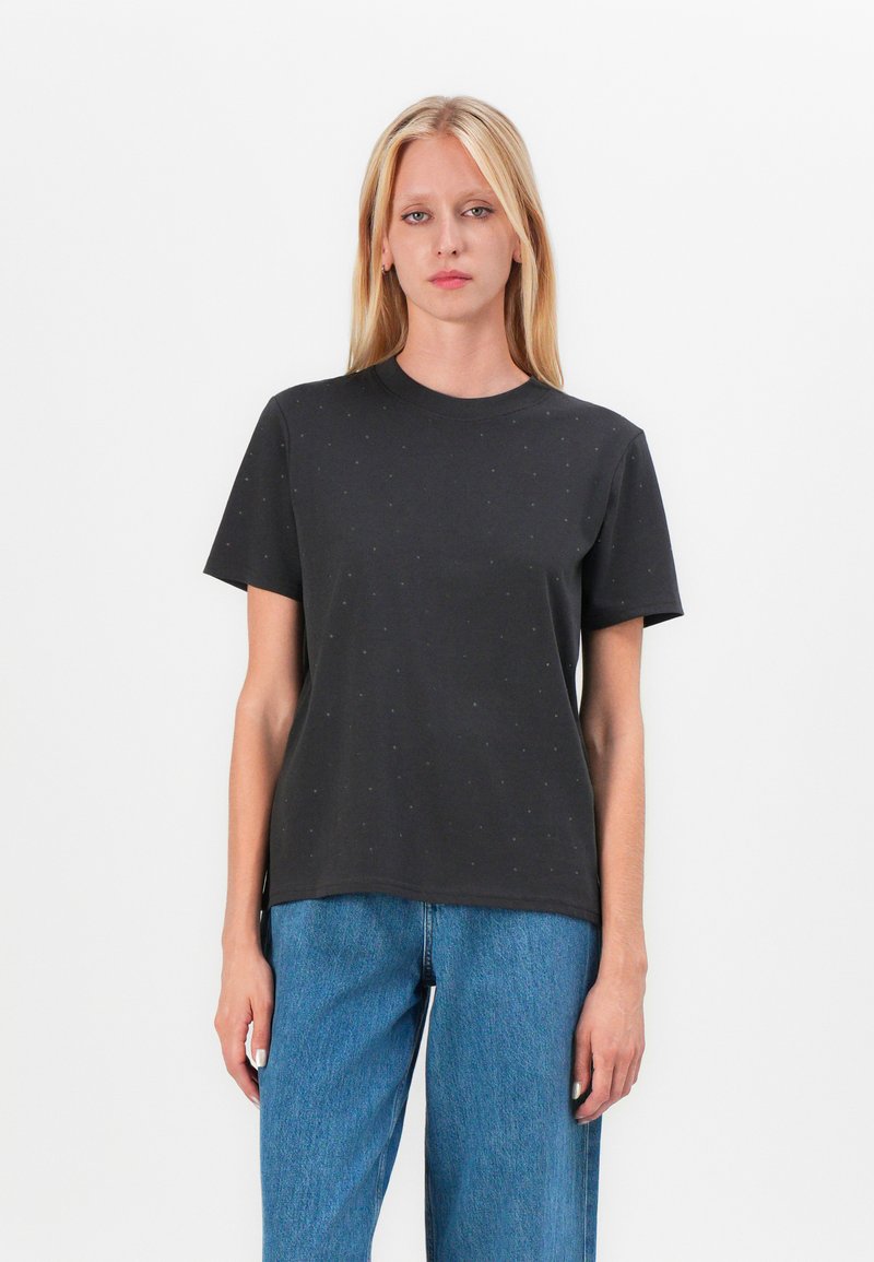 Black cotton t-shirt with short sleeves, round neckline, and subtle dotted pattern across the fabric. Paired with blue denim wide-leg jeans.