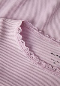 Jasnoróżowy prążkowany top z falbankową koronką na dekolcie, prezentujący miękką fakturę i subtelny wzór, oznaczony metką z rozmiarem.