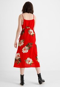 Röd blommig midiklänning med vita och gröna blommor, justerbara spagettistraps och en draperad midja med snörning. Svarta ankelstövlar fulländar looken.