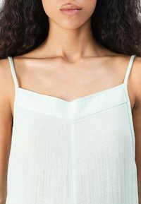 Lichtgroene, mouwloze top van zacht, gestructureerd materiaal met een v-hals en dunne bandjes, voorzien van subtiele verticale lijnen.
