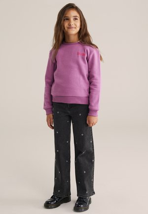 Sweatshirt violet avec des poignets côtelés et un col rond, associé à un jean large noir avec des accents circulaires blancs et des bottes noires.