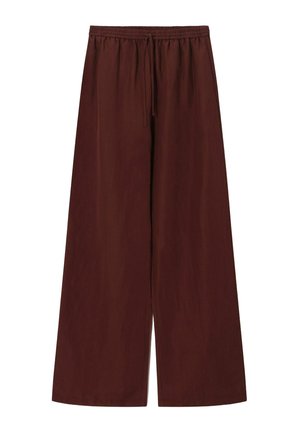 Personne portant un pantalon large marron ample avec une taille à cordon, tenant un haut tricoté rayé rouge, jaune et crème.