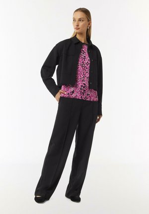 Black cropped jacket over a pink patterned blouse, paired with loose black trousers and black shoes. Smooth textures, contrasting colors.