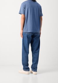 Modré bavlněné tričko s krátkými rukávy, spárované s volně střiženými modrými džínami. Obuv zahrnuje světlé tenisky.