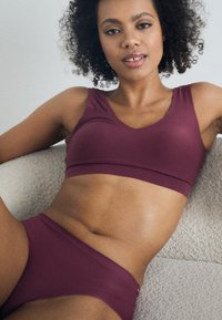 Maroon bra and briefs set made of smooth, stretchy fabric. Bra features a v-neck design; bottoms have a low-rise cut and seamless edges.