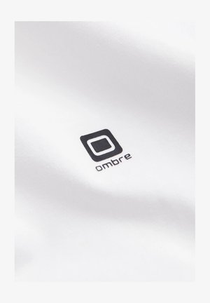 Hvidt stof med et sort logo i kvadratisk omrids og ordet "ombre" skrevet med små bogstaver. Glat tekstur, minimalistisk design.