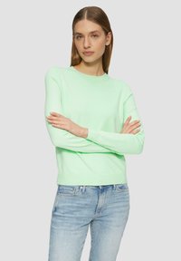 Miętowy sweter dzianinowy z długimi rękawami, okrągłym dekoltem i ściśleżu rękawami, w połączeniu z jasnoniebieskimi dżinsami. Miękka tekstura i dopasowany krój.