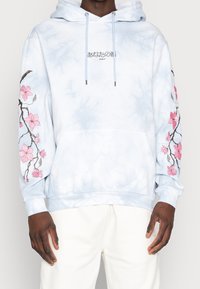 Vaaleansininen t-paita, joka on valmistettu pehmeästä kankaasta ja jossa on kirjaillut vaaleanpunaiset kukat hihoissa sekä mustaa etutekstiä. Mukava istuvuus.