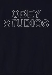 Felpa navy con testo ricamato bianco che recita "OBEY STUDIOS" in lettere maiuscole sul petto. Design semplice, senza motivi.