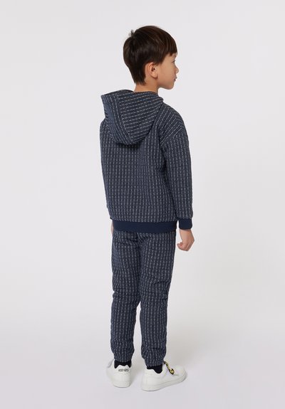 Ensemble de sweat à capuche et pantalon en marine avec un motif rayé texturé, des poignets élastiques et une capuche arrière avec un cordon de serrage. Assorti à des baskets blanches.