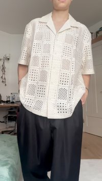 Camicia button-up di colore crema con texture in pizzo, caratterizzata da disegni a giorno, maniche corte e una vestibilità rilassata, abbinata a pantaloni baggy neri.