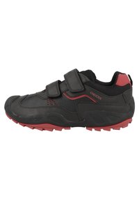Des chaussures de sport noires avec des accents rouges, dotées d'une tige synthétique, de deux bandes Velcro, de côtés texturés et d'une semelle en caoutchouc robuste.