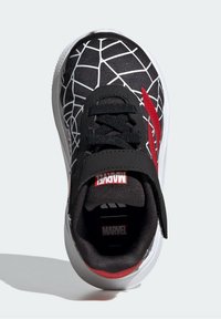 Chaussure de sport noire avec un motif en toile, des accents rouges et une sangle à boucle. Présentant une semelle rembourrée et un col matelassé pour le confort.