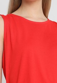 Czerwony top bez rękawów wykonany z gładkiej bawełny, z okrągłym dekoltem i luźnym krojem, o prostych i czystych liniach.