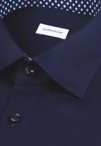 Camicia blu navy con colletto rigido, con un motivo a pois a contrasto all'interno. Etichetta con scritto "seidensticker". Texture morbida.