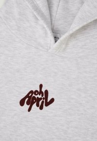 Pelēka kapuce ar priekšējo kabatu un kapuci. Centrā ir redzams izteiksmīgs brūns grafiskais teksts "oh April". Mīksta, teksturēta auduma.