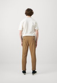 Light beige short-sleeve shirt and brown tapered pants with rolled cuffs. Black sneakers with white accents. Plain background.