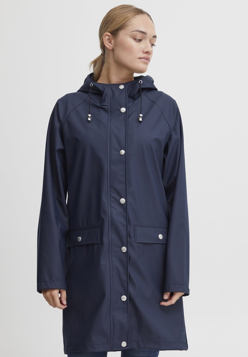 Navy waterproof raincoat with a front zipper, snap closures, adjustable hood, and two front pockets. Smooth texture with a relaxed fit.